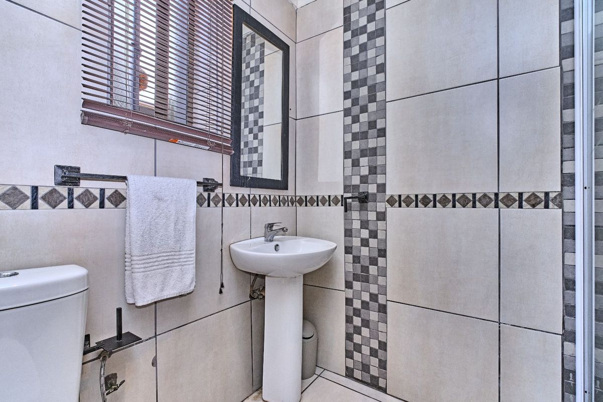 A compact bathroom featuring a pedestal basin, toilet, and tiled walls with decorative mosaic accents and a window with fitted blinds.