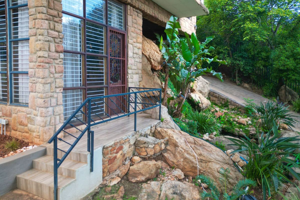 A rustic exterior view featuring natural stone cladding, a tiled entrance staircase with metal railings, and integrated landscaping with large rock formations.