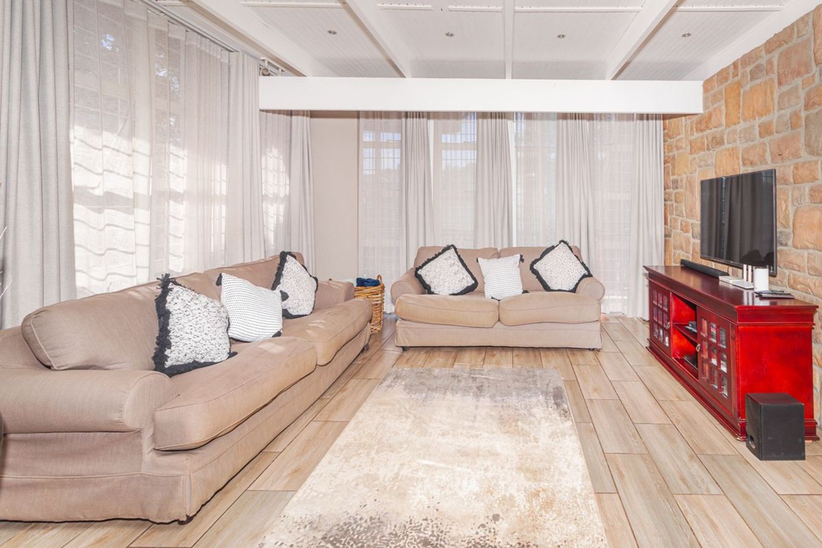 A bright living room featuring a rustic stone feature wall, wood-look tiled flooring, and a beamed ceiling with recessed lighting.