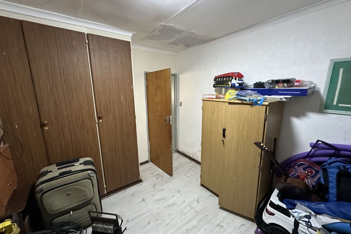 A bedroom featuring built-in wooden cupboards, laminate flooring, and visible signs of ceiling water damage and wall moisture.