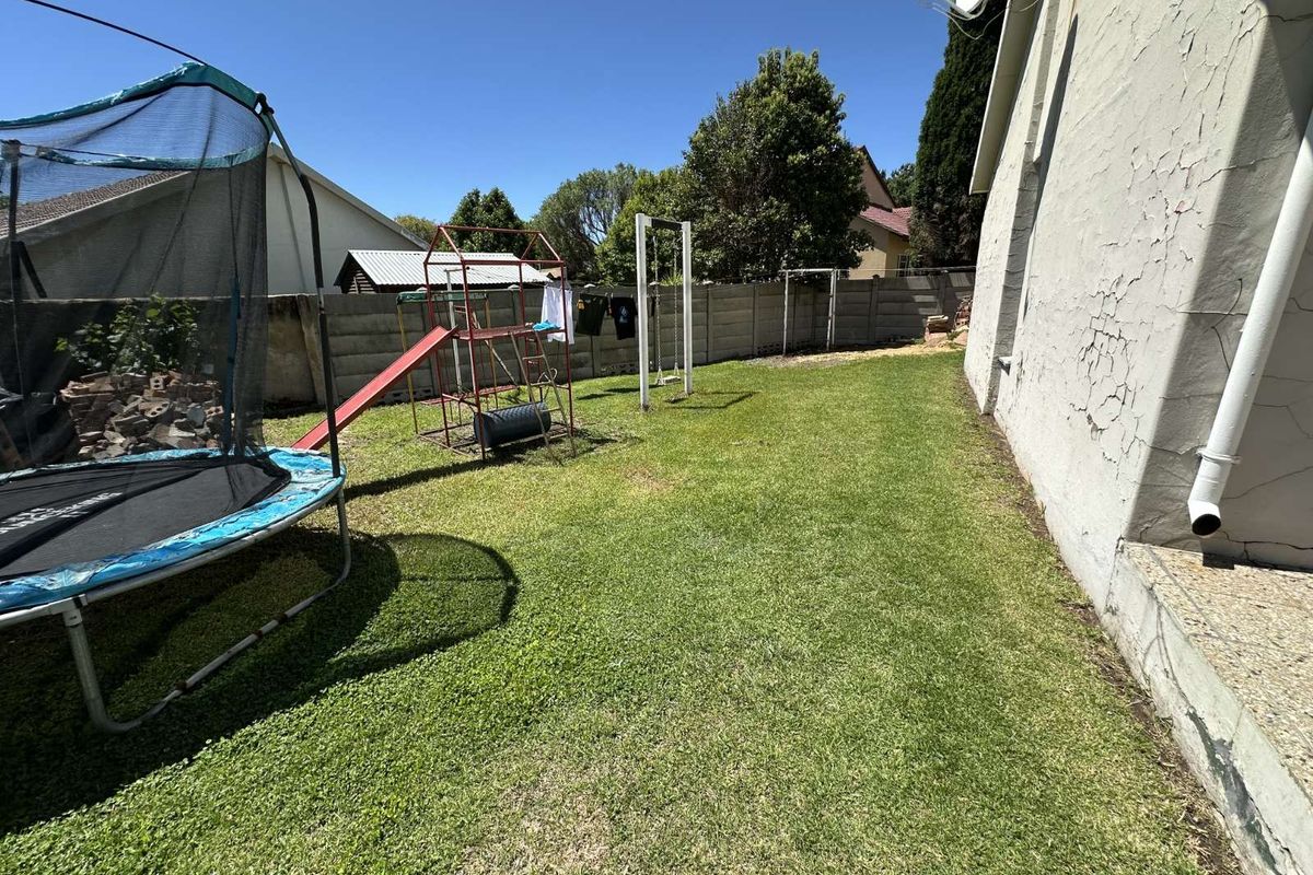 A rear garden area featuring a lawn, perimeter boundary wall, and exterior wall access to the main house structure.
