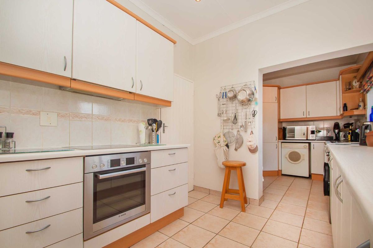 A functional kitchen featuring white cabinetry, built-in oven, ceramic cooktop, and tiled flooring, with an adjoining scullery area for additional utility.
