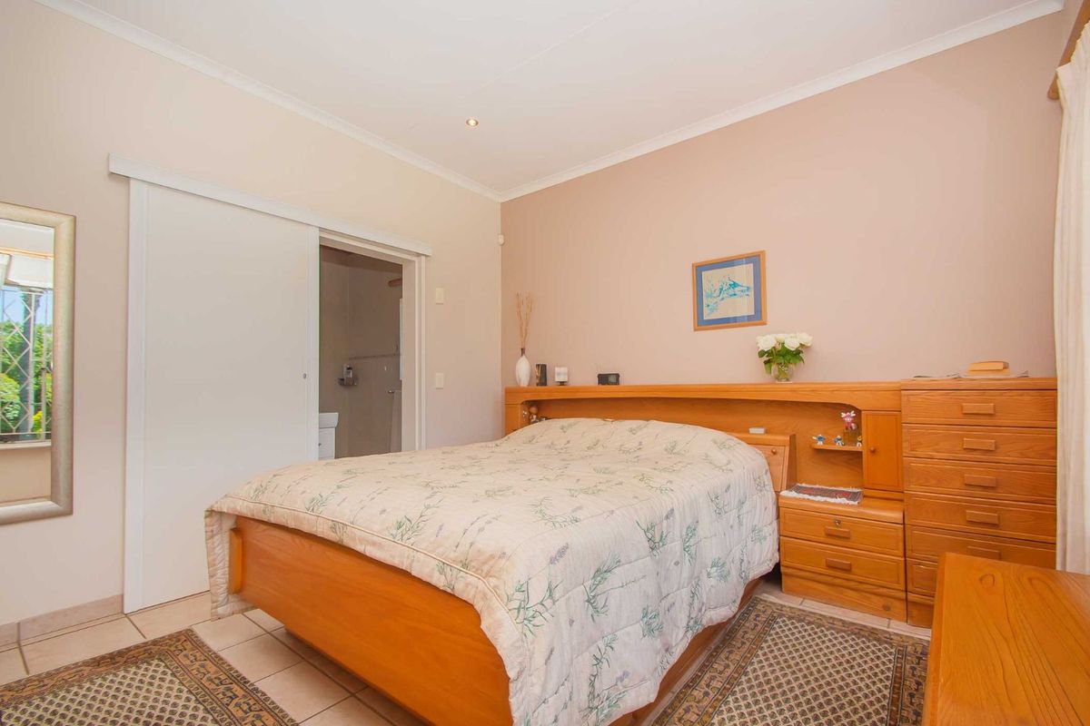 A well-maintained bedroom featuring built-in wooden headboard cabinetry and an en-suite bathroom access via a sliding door.