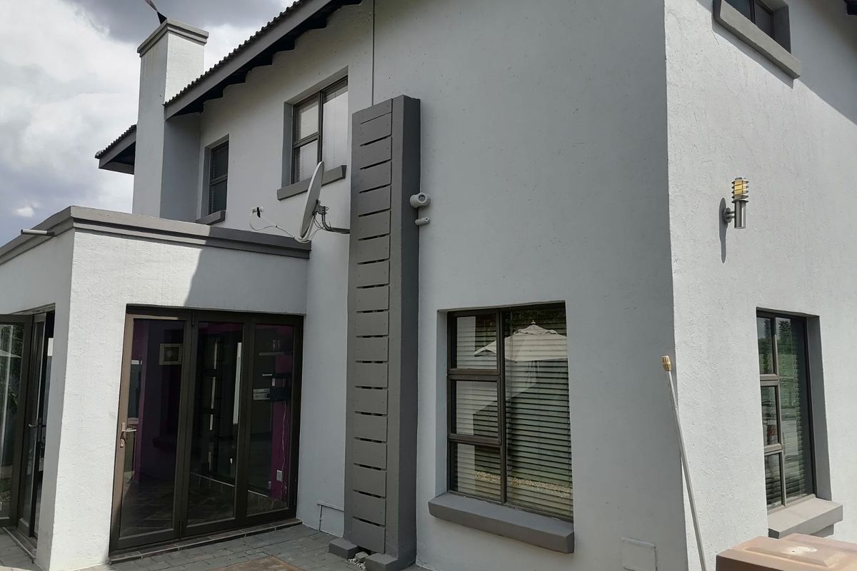 A view of the rear exterior elevation featuring a paved patio area, modern aluminium-framed windows, and a chimney stack.