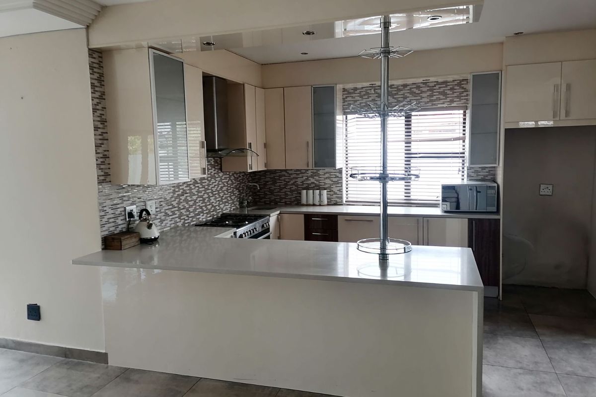 Modern kitchen featuring a breakfast bar, stone countertops, mosaic tile backsplash, built-in cabinetry, and stainless steel extractor fan.