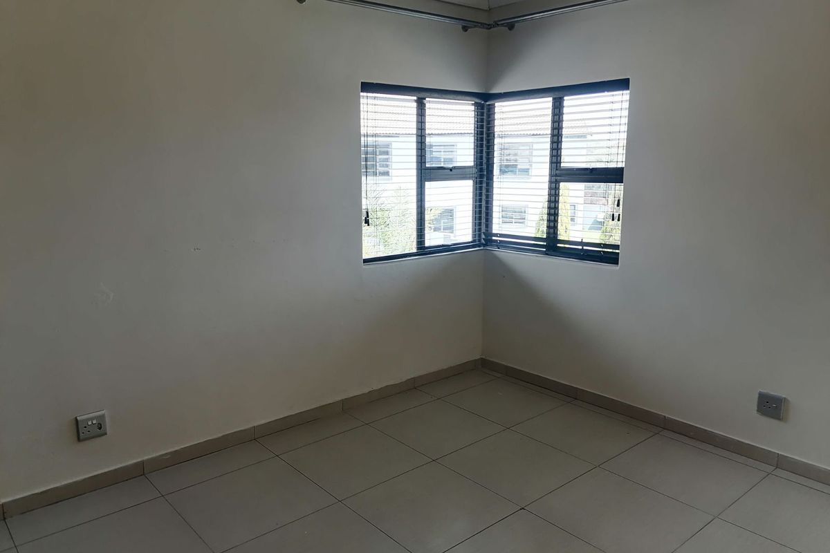 A bright, empty bedroom featuring neutral floor tiles, corner windows with fitted blinds, and curtain rods installed.