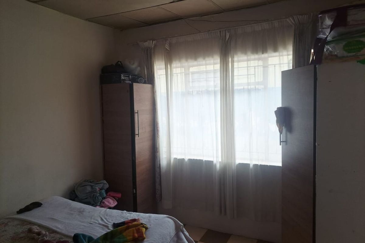 A bedroom featuring tiled flooring, a window with security bars, and a drop ceiling.