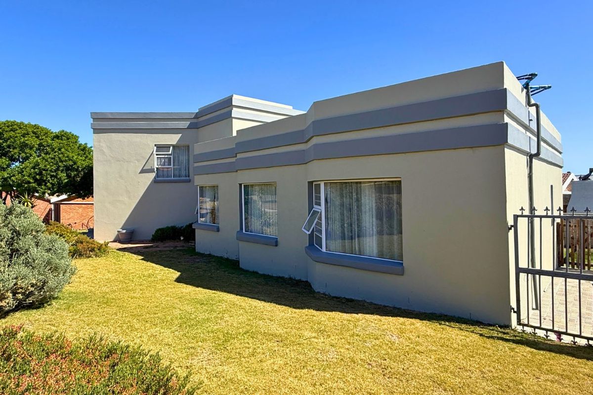 A view of the exterior side elevation of the house, featuring painted masonry walls, metal-framed windows, and a manicured lawn.