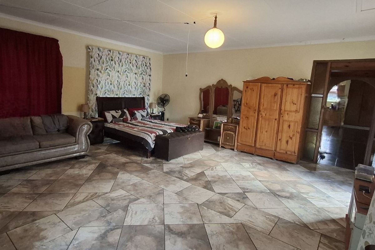 Spacious bedroom featuring large format floor tiles, neutral wall tones, and direct access to an adjoining hallway.