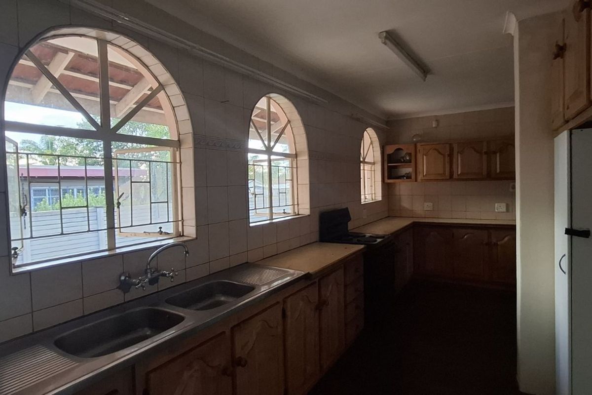 A dated kitchen featuring wooden cabinetry, double basin sink, and arched windows. The space offers a functional layout with potential for modern renovation.