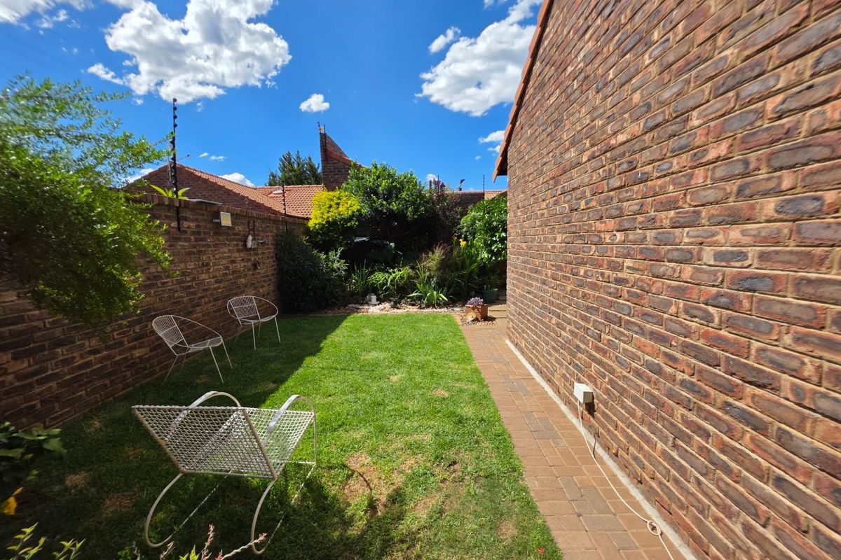 A private rear garden featuring a manicured lawn, brick boundary walls, and a paved walkway alongside the exterior brick wall of the house.