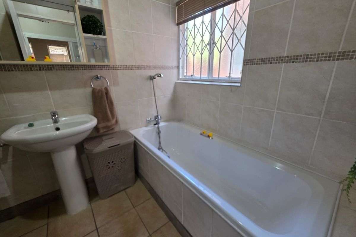 A functional bathroom featuring a white bathtub with shower mixer, pedestal basin, and tiled walls with a decorative mosaic border.