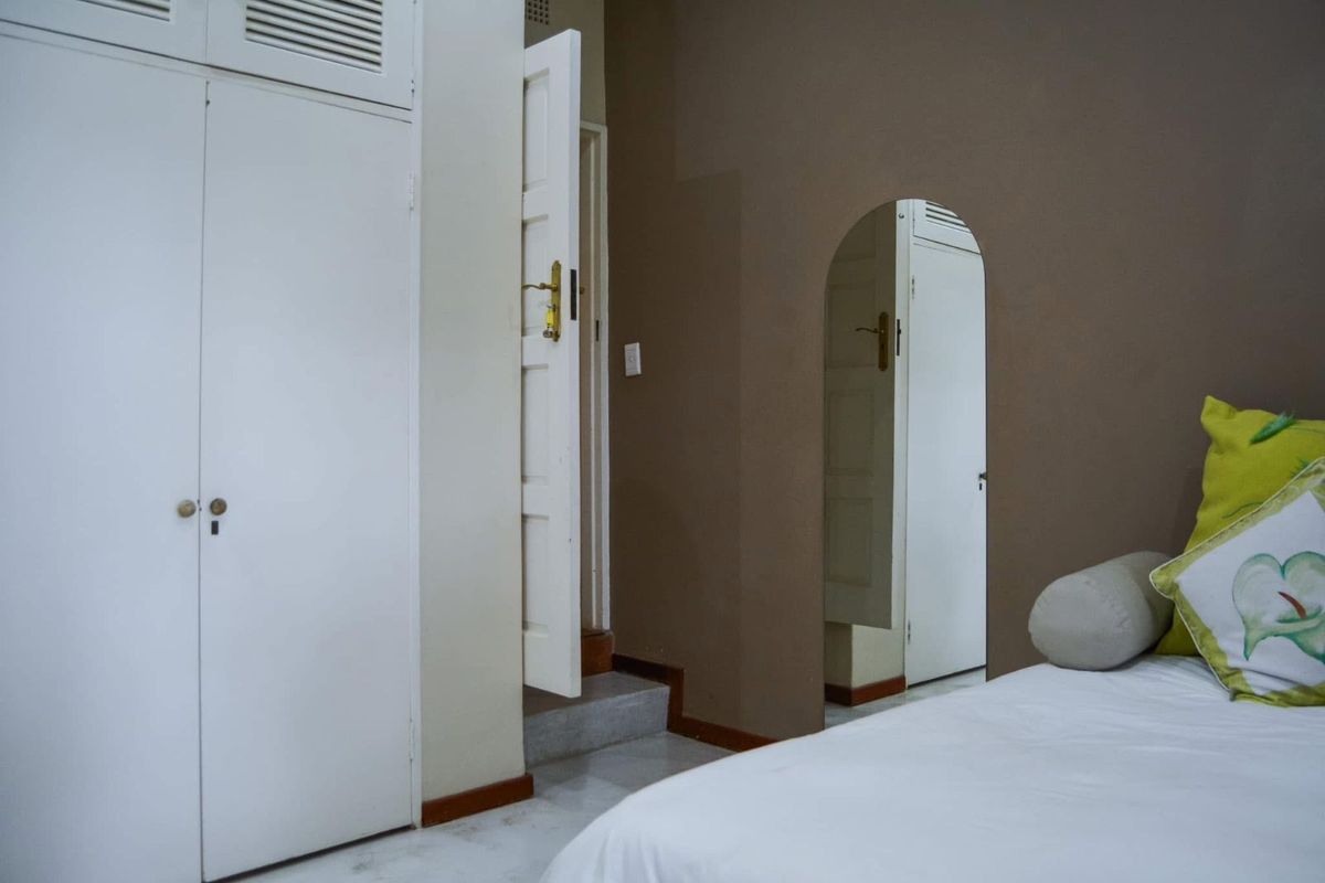 A bedroom featuring built-in white cabinetry, a neutral brown accent wall, and an arched doorway leading to an adjacent space.