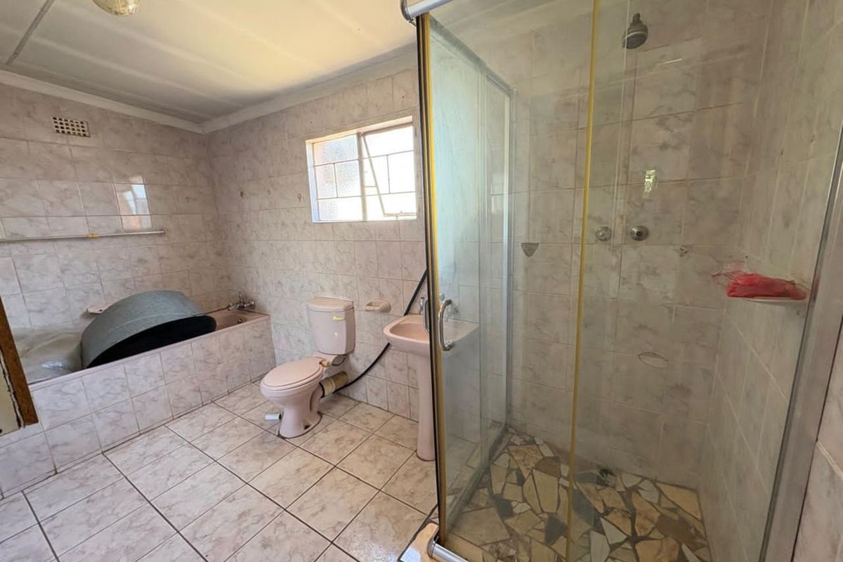 A dated bathroom featuring a tiled shower enclosure, pedestal basin, toilet, and a built-in bathtub with full wall tiling.