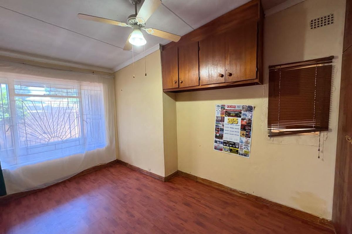 A bedroom featuring wood-look laminate flooring, a ceiling fan, and built-in wooden overhead cabinetry.