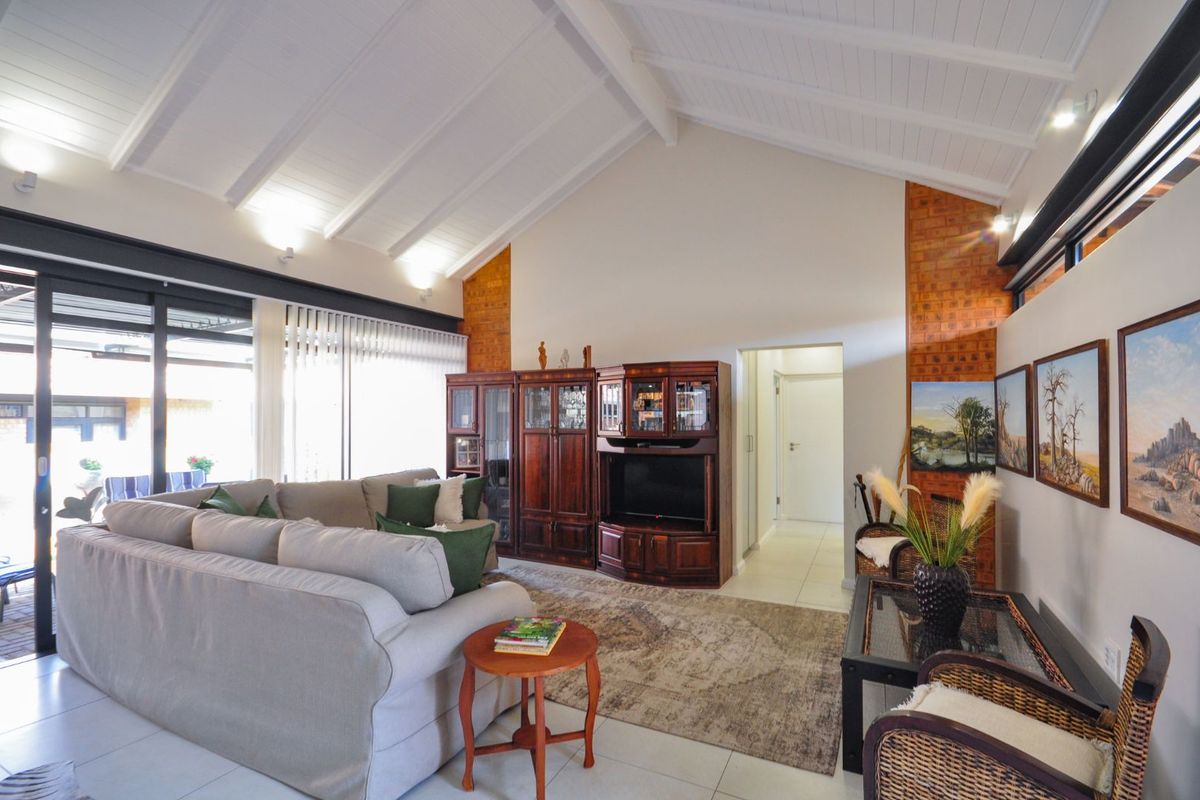 Spacious living area featuring high vaulted ceilings with exposed beams, tiled flooring, and large sliding glass doors providing access to the patio.