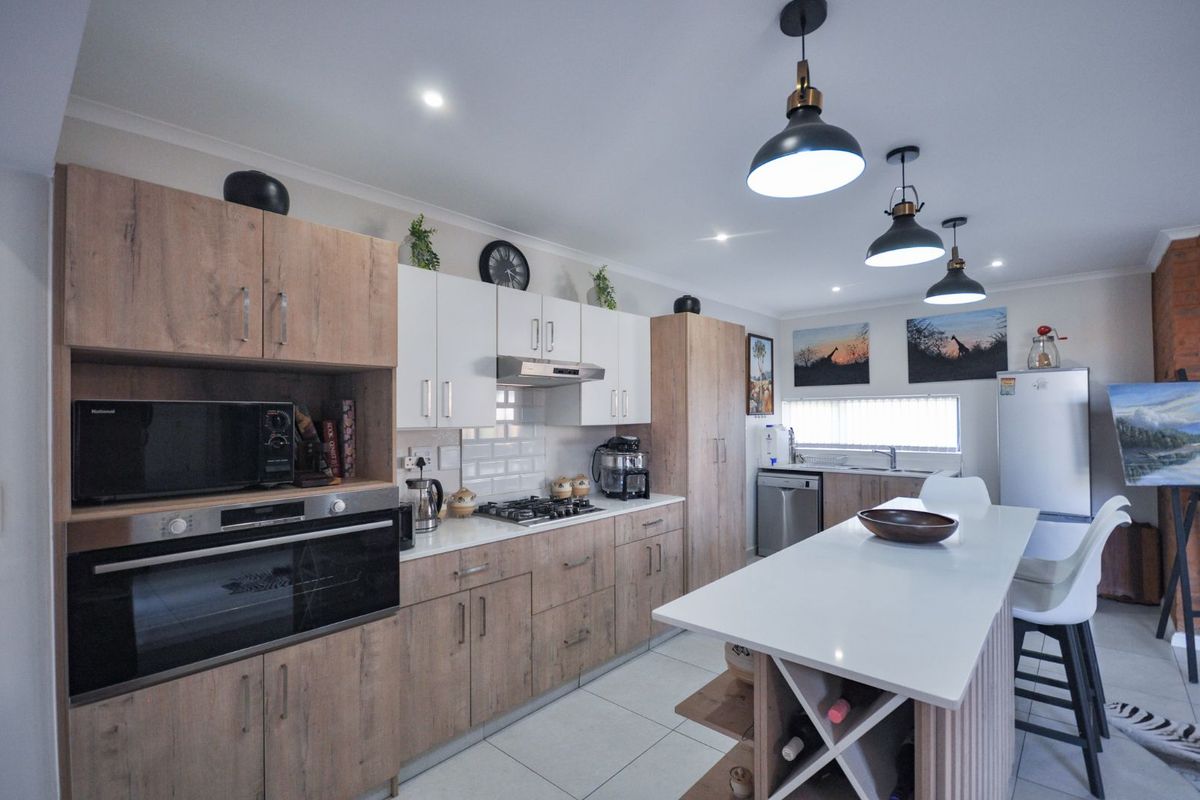 Modern kitchen featuring wood-grain and white cabinetry, stone countertops, a gas hob, built-in oven, and a central island with integrated wine storage.