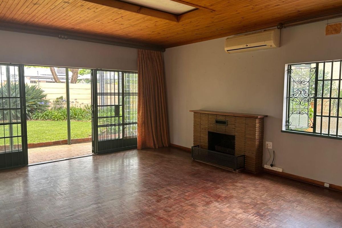Spacious living room featuring parquet flooring, a built-in brick fireplace, and sliding glass doors opening to a private garden.