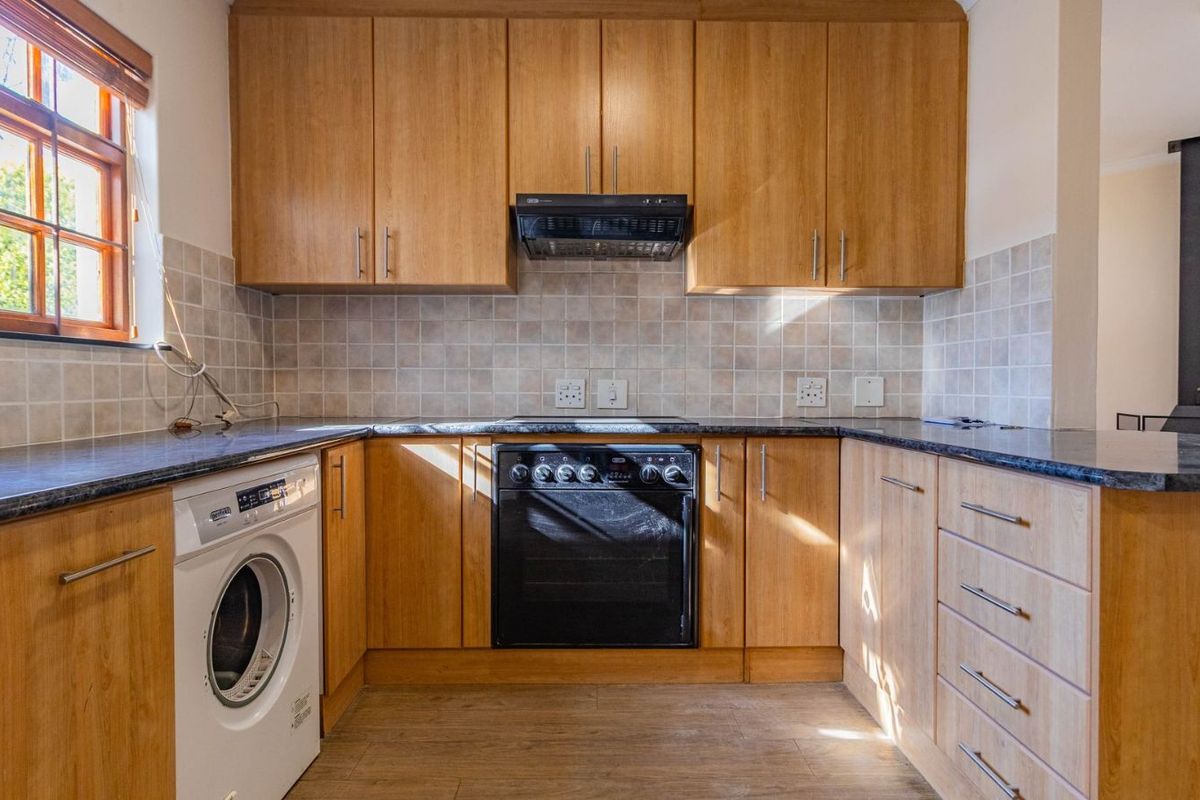 A functional kitchen featuring wood-finish cabinetry, dark countertops, tiled backsplash, built-in oven with extractor fan, and space for a washing machine.