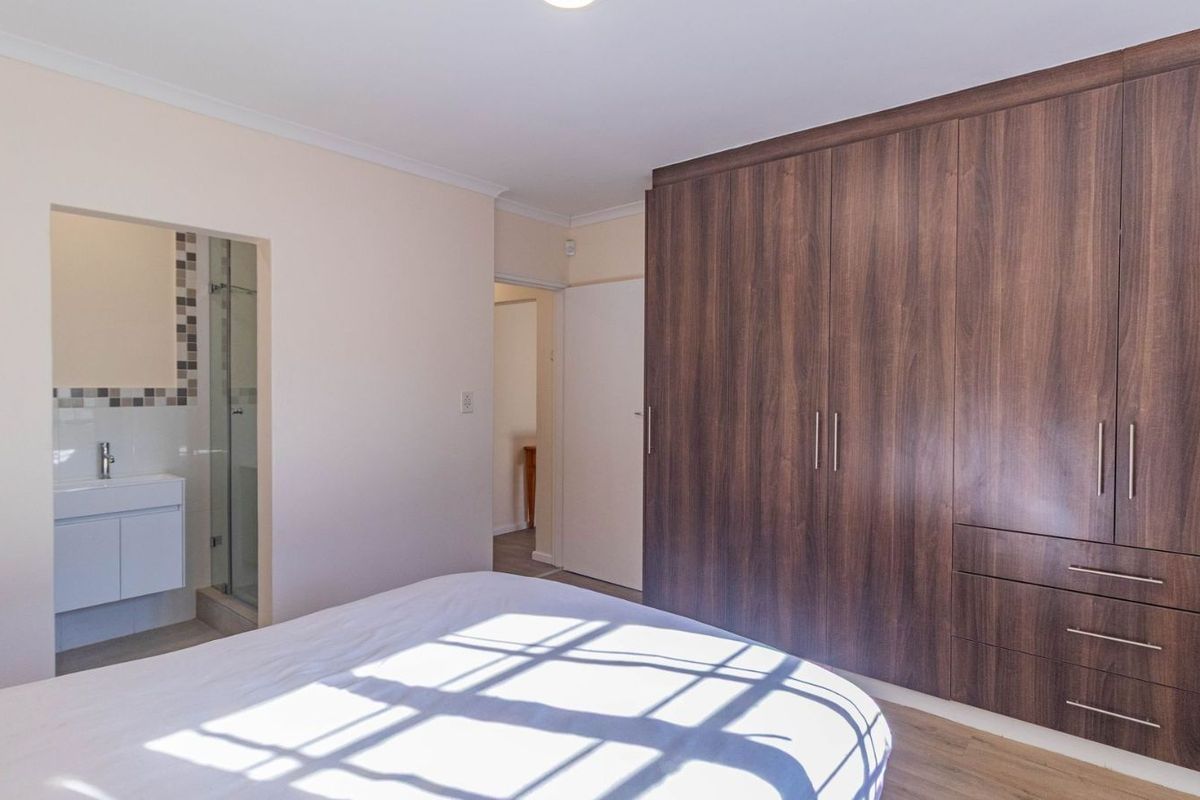 A well-maintained bedroom featuring extensive built-in wooden cabinetry and an en-suite bathroom with a modern vanity and glass-enclosed shower.