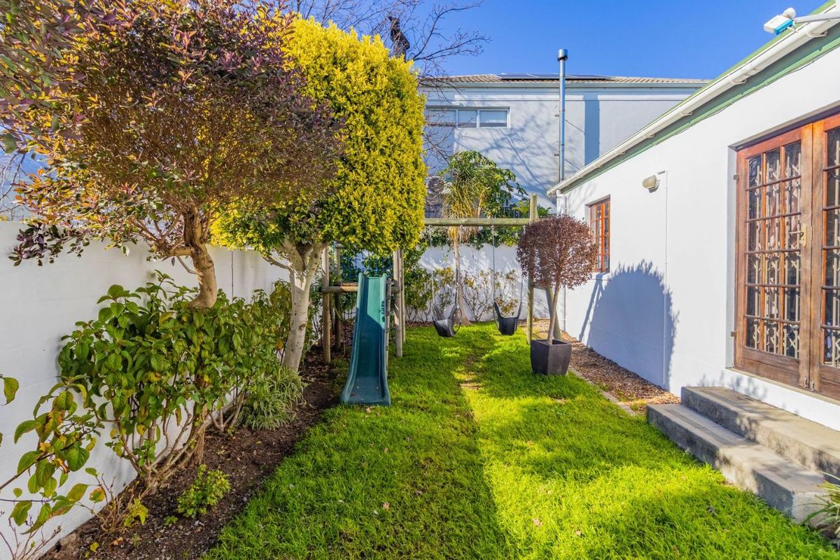 A private rear garden featuring a lawn, established landscaping, and direct access to the home via timber-framed glass double doors.