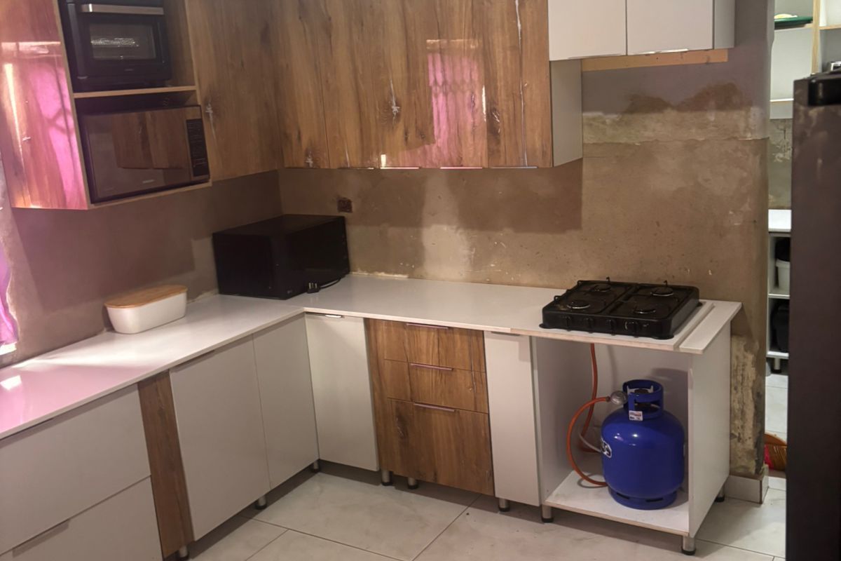 A kitchen featuring modern two-tone cabinetry, white countertops, and tiled flooring, currently requiring final wall finishes and backsplash installation to complete the space.