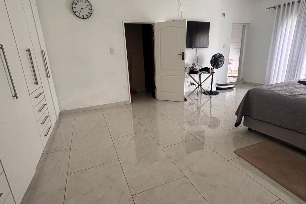 Spacious bedroom featuring large format floor tiles, extensive built-in cabinetry, and direct access to an adjoining room.