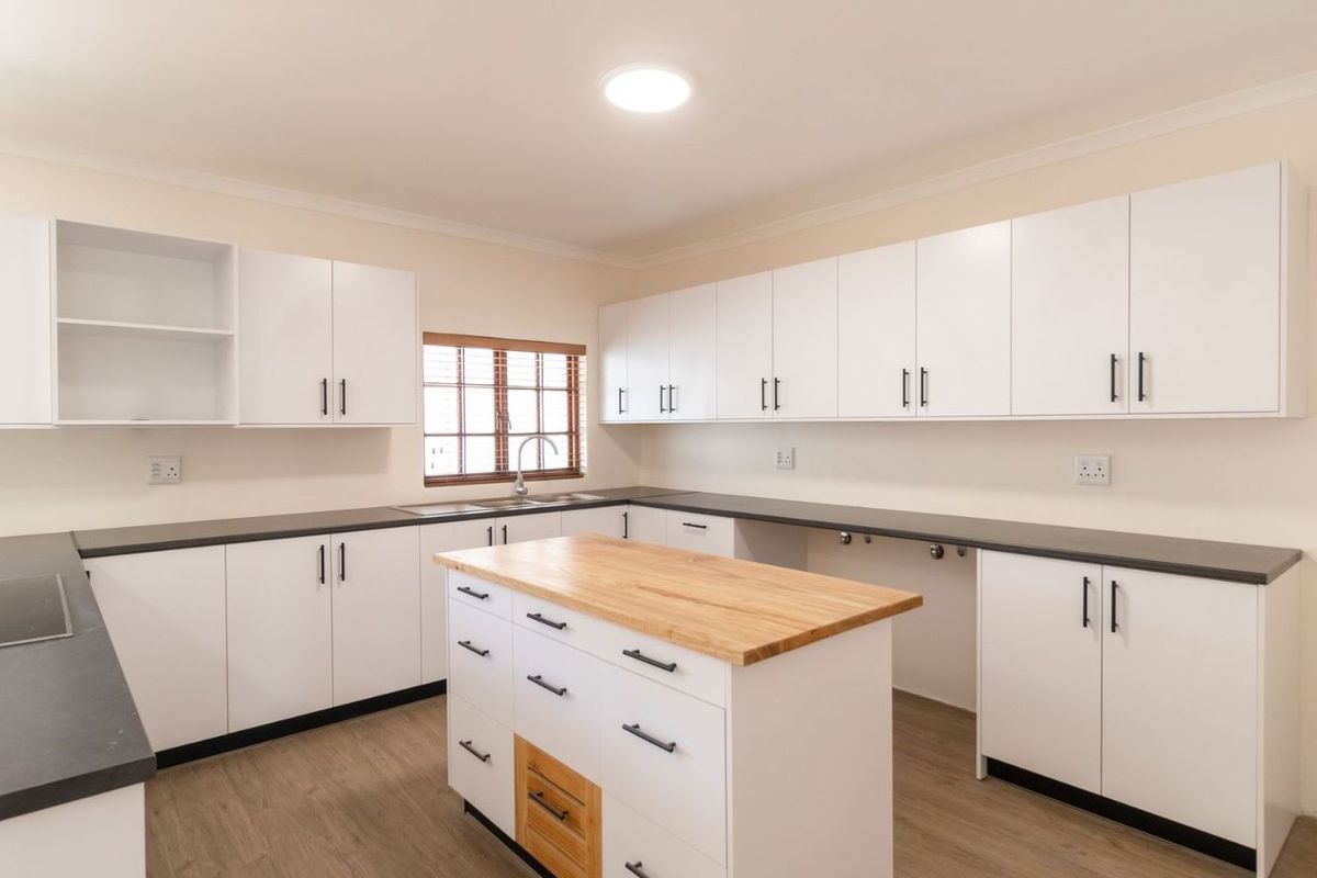 Modern kitchen featuring white cabinetry, dark countertops, a central island with a wooden top, and integrated cooktop.