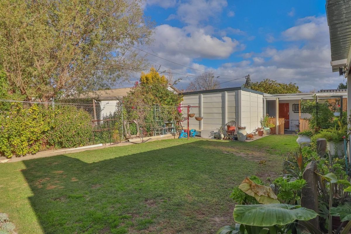 A spacious rear garden featuring a lawn area, established perimeter hedging, and a detached outbuilding with a covered walkway.