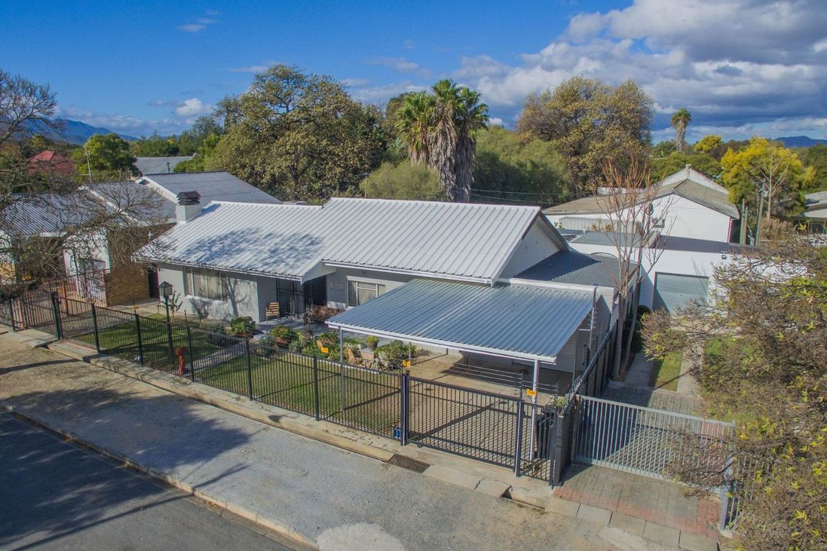 Aerial view of a residential property featuring a metal roof, carport, secure perimeter fencing, and a paved driveway.
