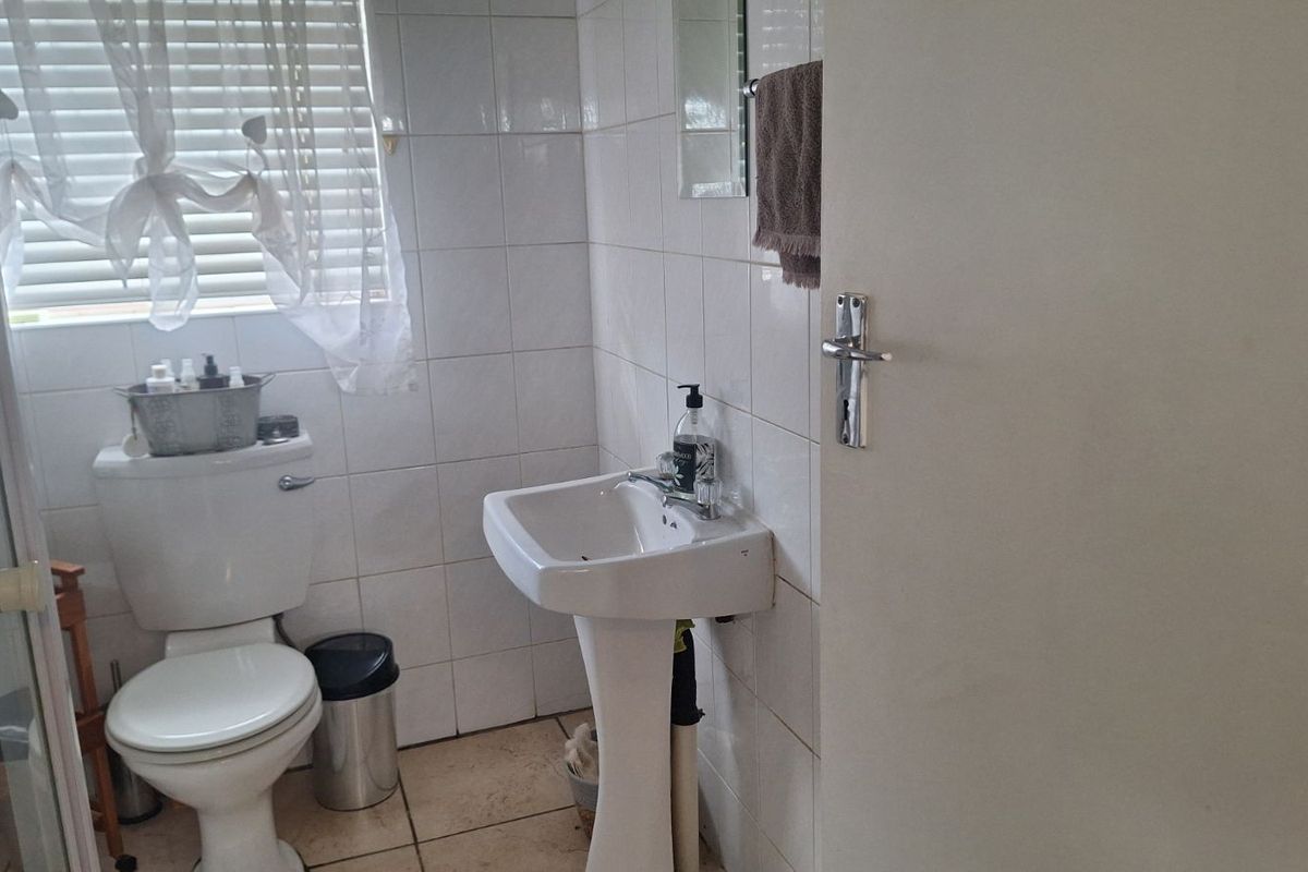 A functional bathroom featuring a pedestal basin, a standard toilet, and a shower enclosure with white wall tiling.