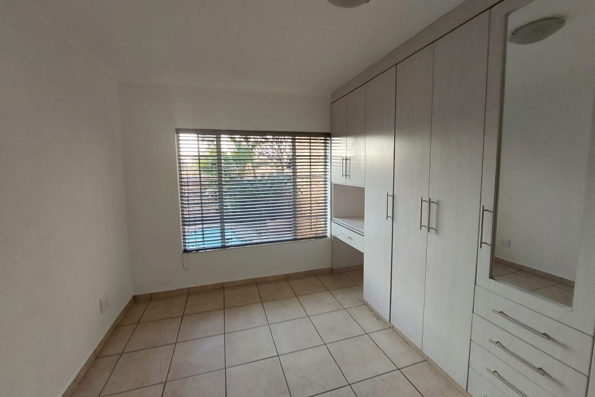 A bright bedroom featuring neutral floor tiles, built-in cupboards with integrated vanity space, and horizontal window blinds.