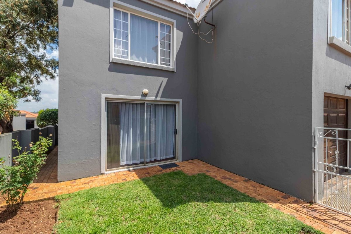 A view of the townhouse rear exterior featuring a small private garden, paved walkway, and sliding glass door access.