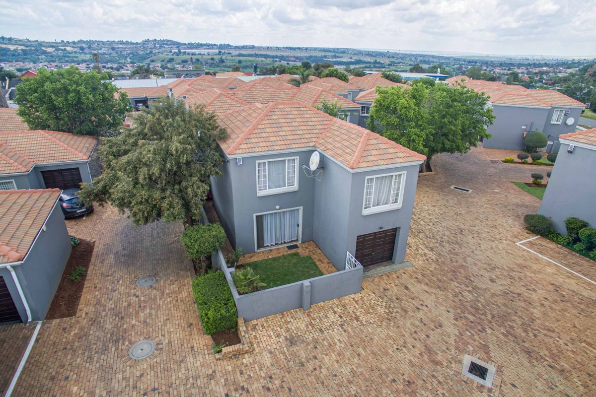 Aerial view of a townhouse complex featuring paved driveways, terracotta tiled roofs, and private garden spaces.