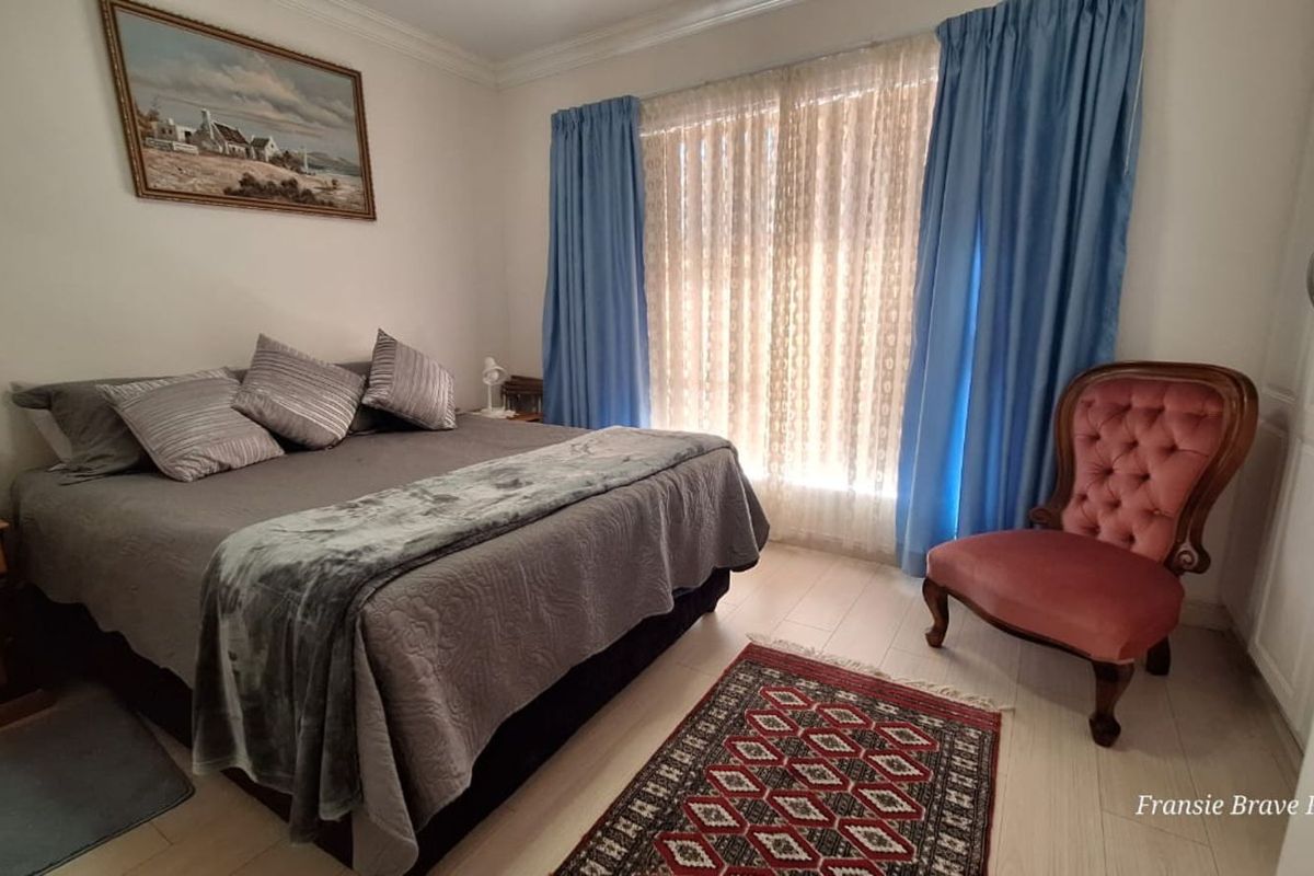 A well-lit bedroom featuring light-toned flooring, built-in wardrobe storage, and large windows dressed with curtains.