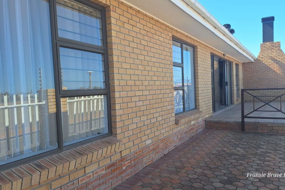 A rear exterior view of the townhouse featuring a paved patio area, brick facade, and a built-in outdoor fireplace.