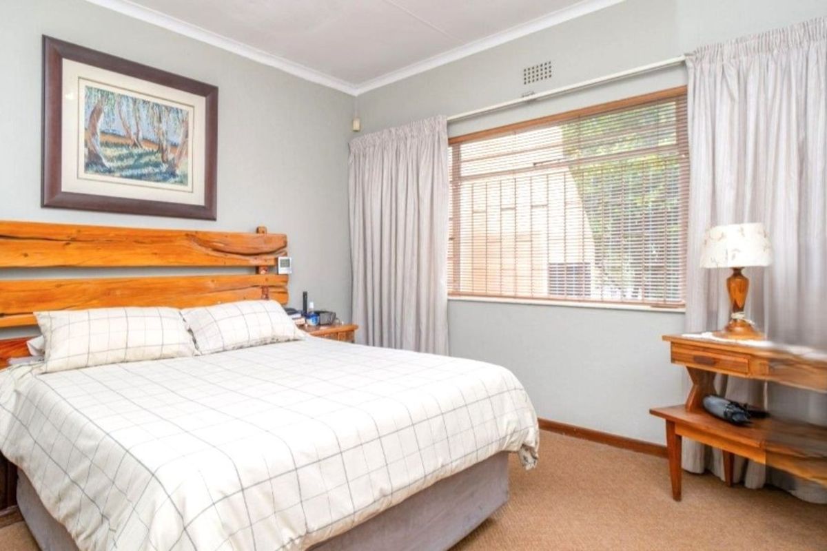 A well-maintained bedroom featuring neutral wall tones, carpeted flooring, and a large window with fitted blinds and curtains.