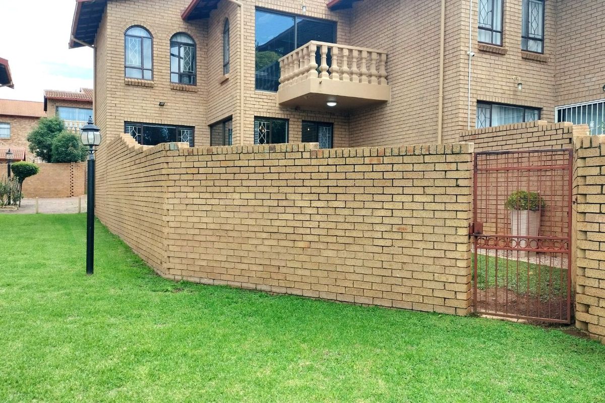 Exterior view of a townhouse featuring a face-brick facade, a private garden area, a balcony, and a secure metal gate entrance.