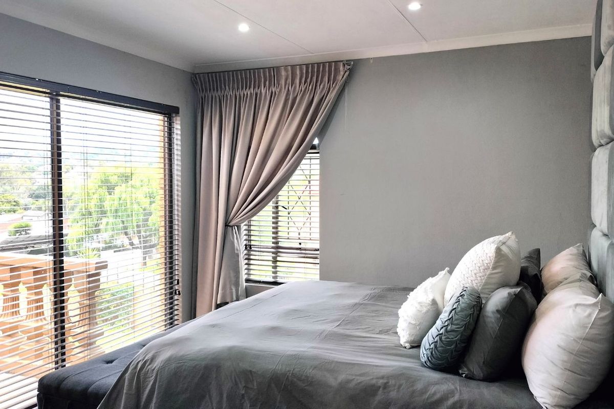 A well-maintained bedroom featuring large windows with fitted blinds, neutral wall finishes, and recessed ceiling lighting.