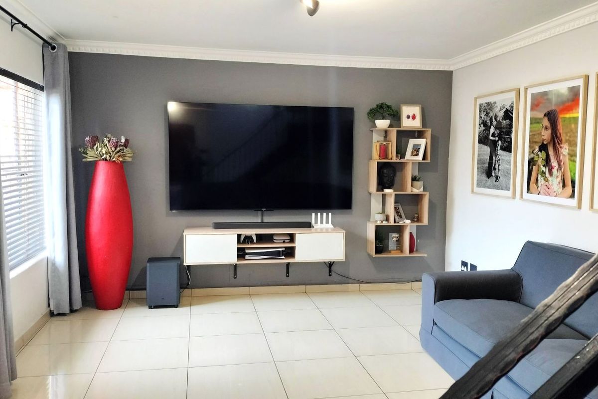 A well-maintained living room featuring large format floor tiles, decorative crown molding, and a feature wall with a wall-mounted media console.