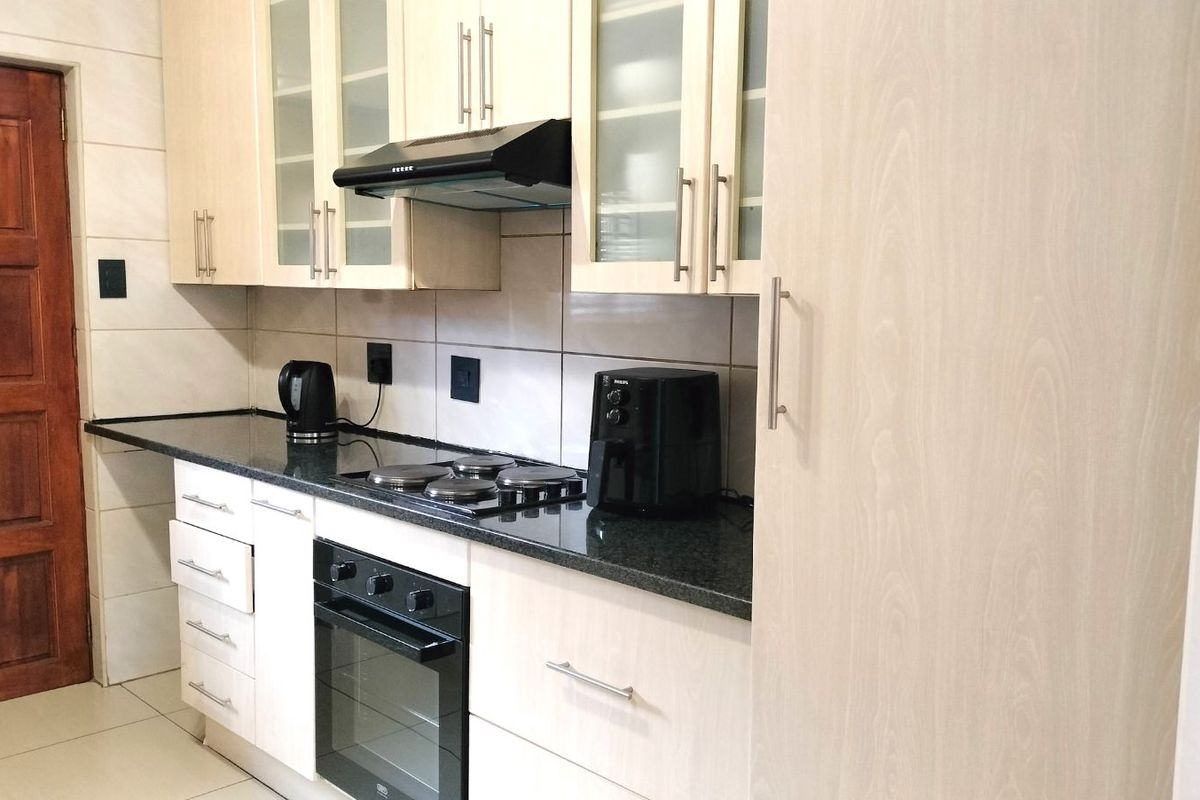 A functional kitchen featuring light wood-grain cabinetry, dark granite countertops, a built-in oven, and a black extractor fan.