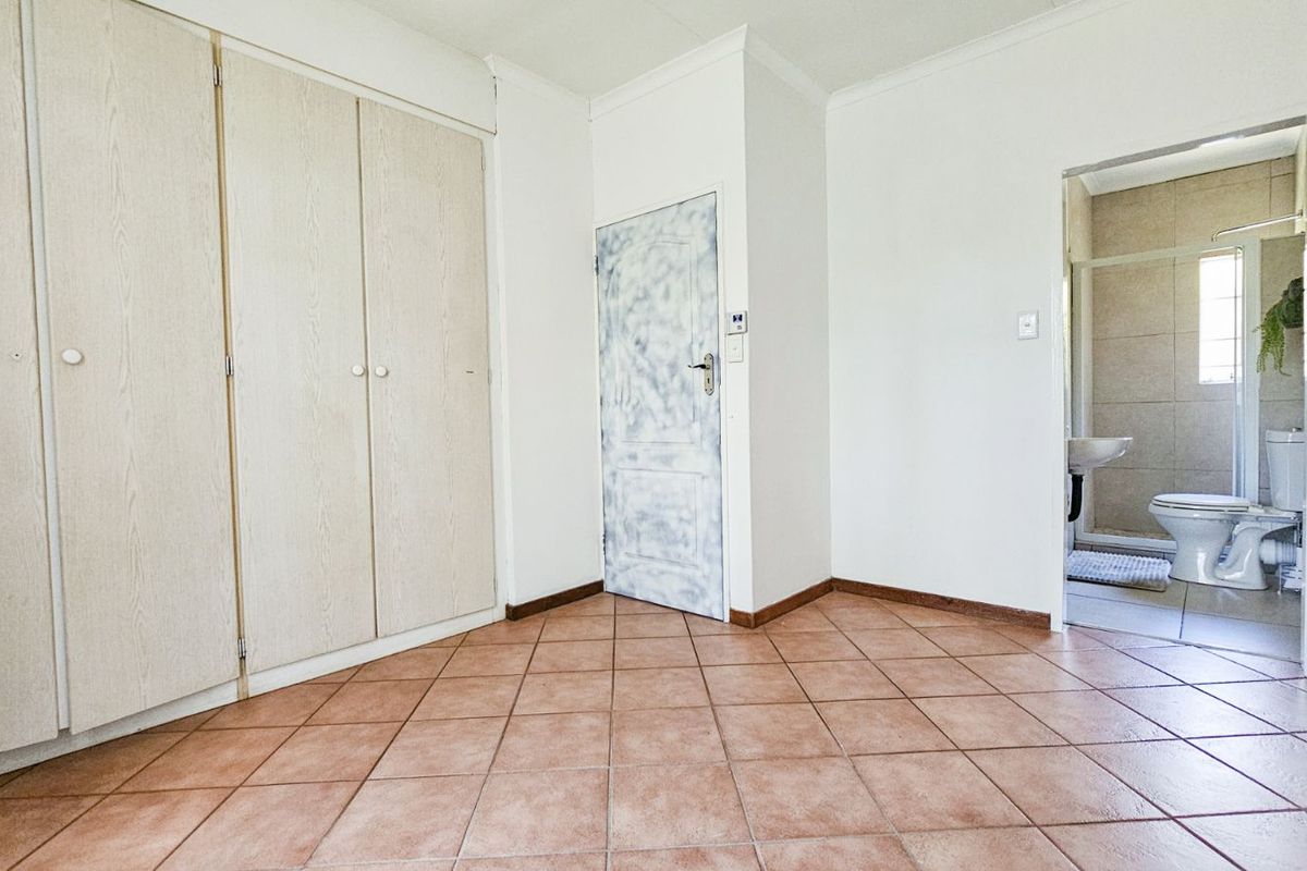 A bedroom featuring built-in cupboards, tiled flooring, and an en-suite bathroom with a toilet and basin.