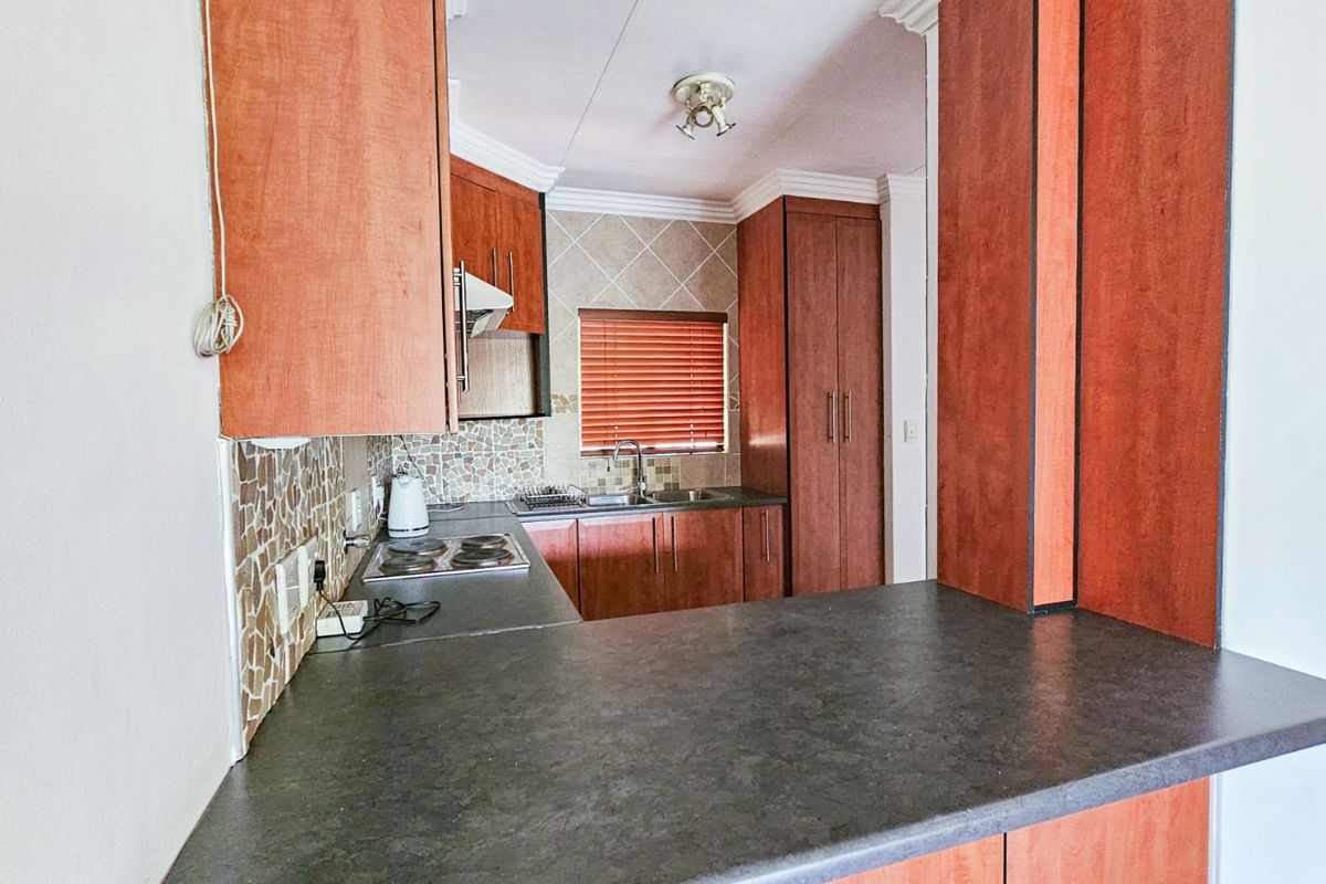 A functional kitchen featuring wood-finish cabinetry, dark laminate countertops, a built-in hob, and a tiled backsplash.