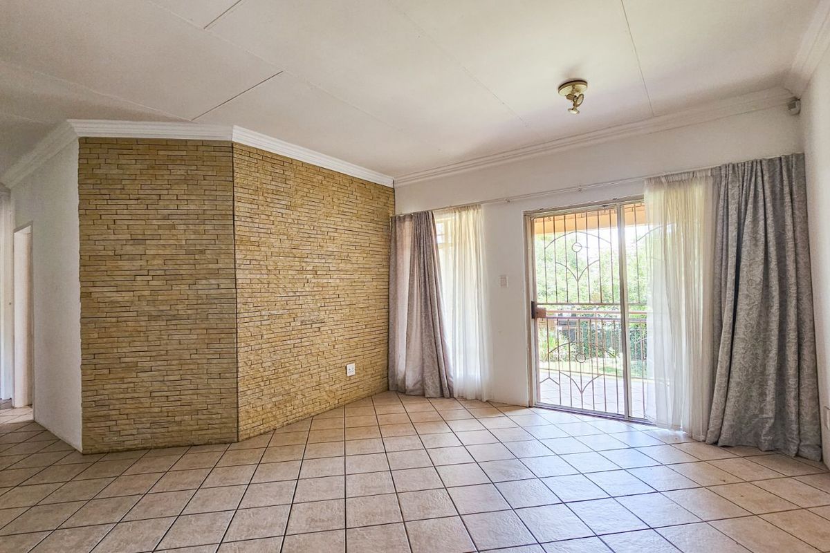 Spacious living area featuring a textured stone feature wall, ceramic floor tiles, and sliding glass doors with security gate leading to the exterior.