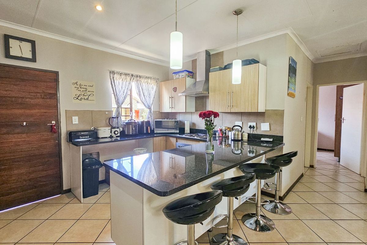 A functional kitchen featuring granite countertops, a breakfast bar, built-in cabinetry, and a stainless steel extractor fan, finished with tiled flooring.