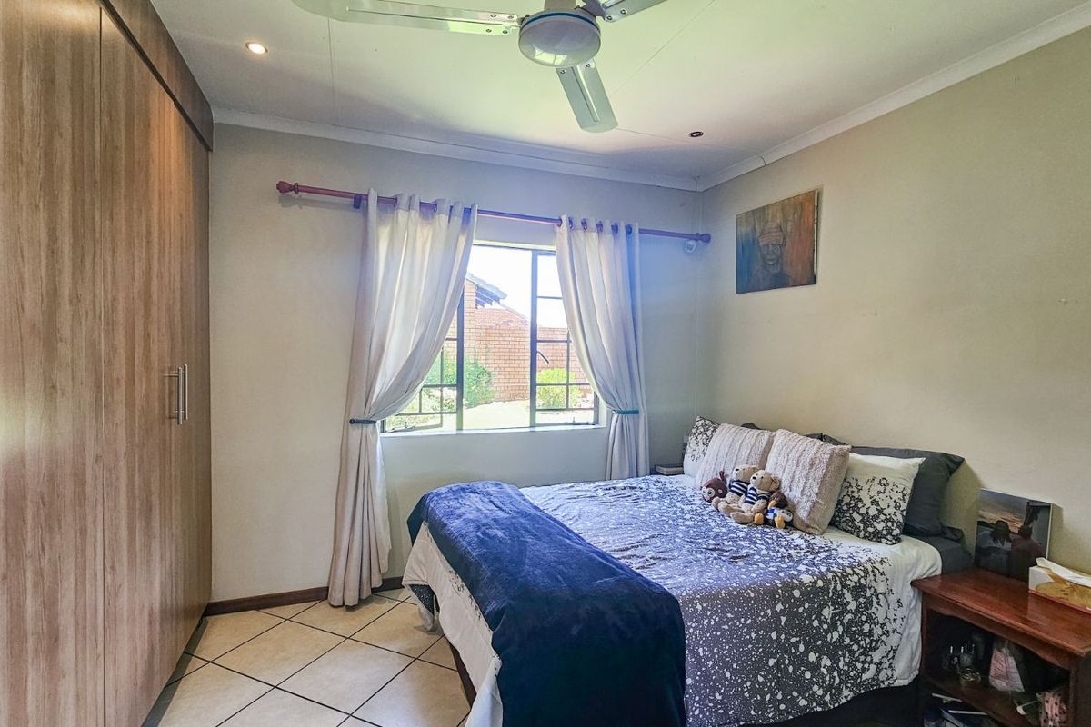 A bedroom featuring built-in wooden cupboards, tiled flooring, and a ceiling fan, offering a functional and comfortable living space.