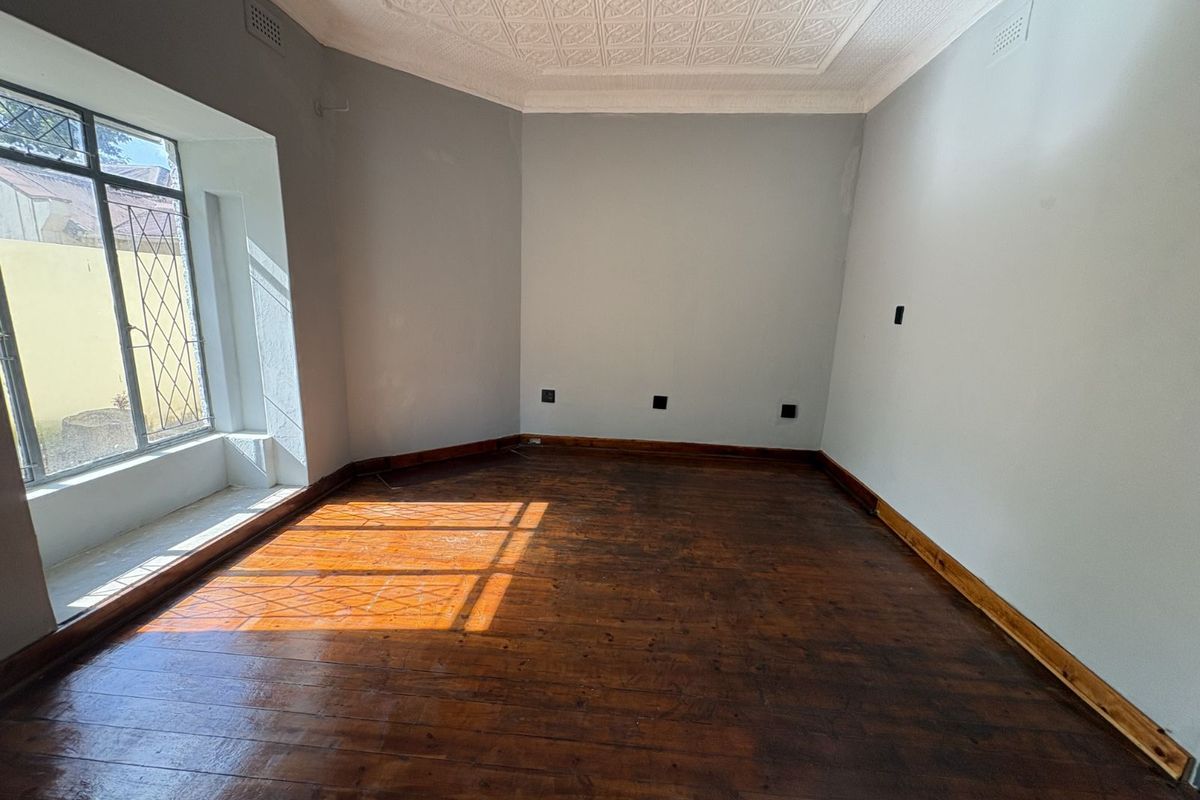 A bright, empty bedroom featuring original polished timber flooring, decorative pressed metal ceiling, and large windows allowing for ample natural light.