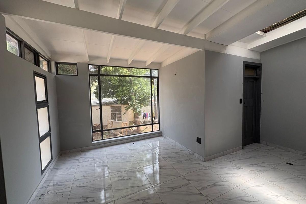 A bright, empty living area featuring large windows, modern marble-look floor tiles, and an exposed beam ceiling design.