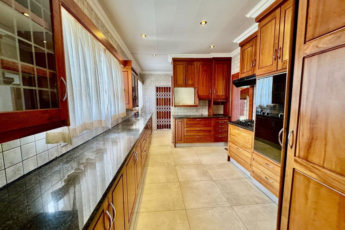 A spacious kitchen featuring extensive wooden cabinetry, granite countertops, tiled flooring, and built-in oven and hob appliances.