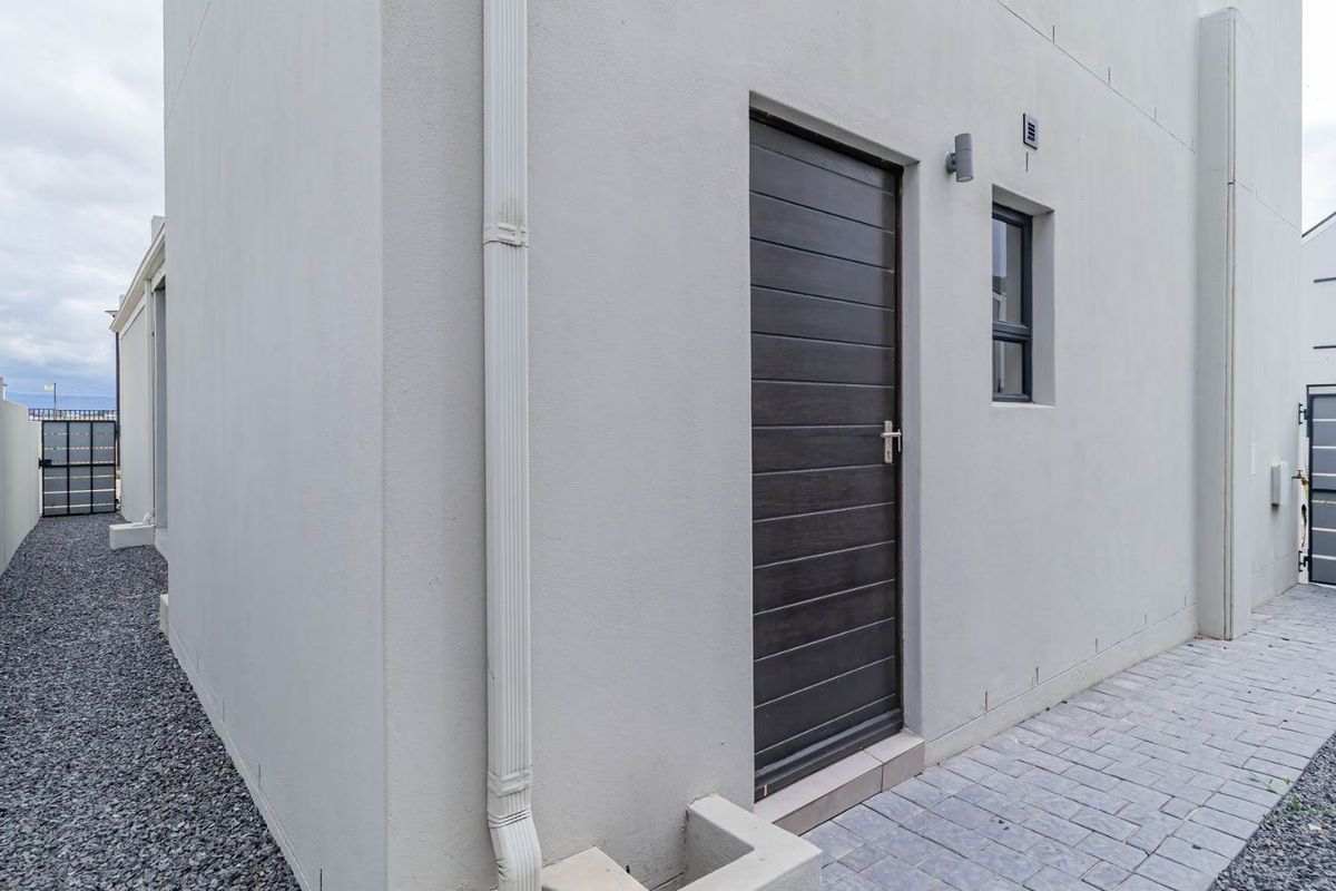 Side exterior view of the townhouse featuring a dark timber-look door, paved walkway, and gravel side passage.